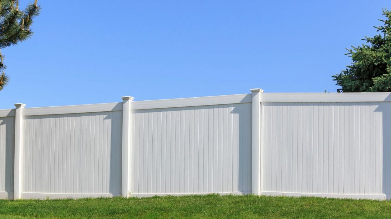 Tall white fence with green grass and a bright blue sky in the back